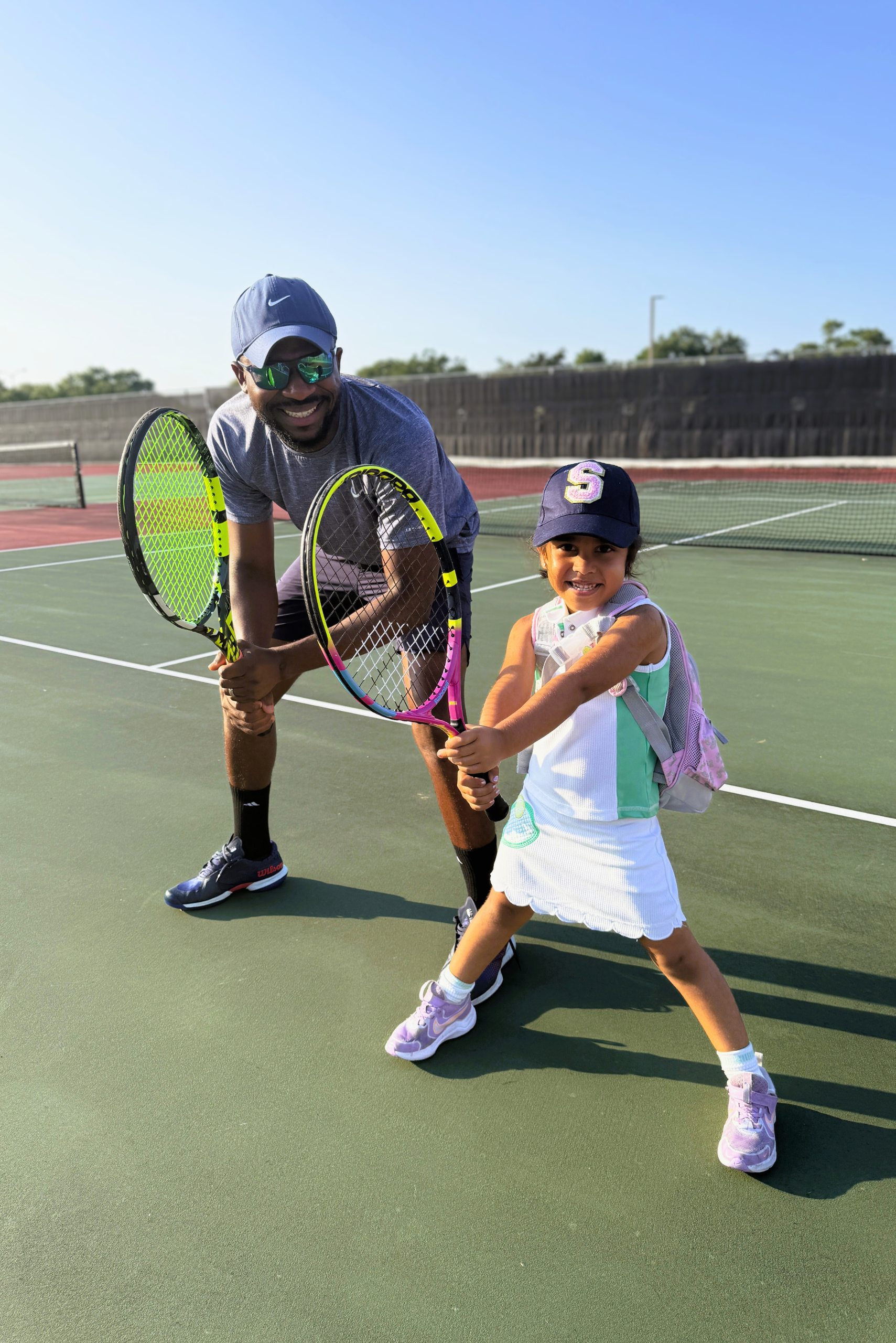 A coach helps a young girl hold her tennis racket correctly during a fun, sunny day of tennis lessons on the court.
