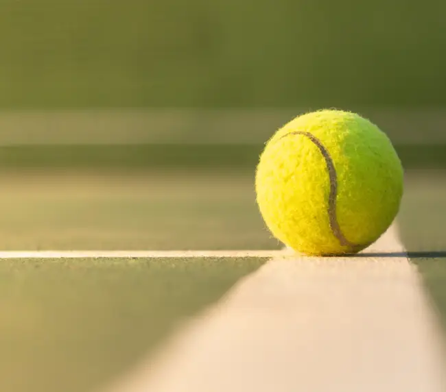 A close-up of a tennis ball on the baseline of a court, illustrating the rich history and evolution of tennis equipment.