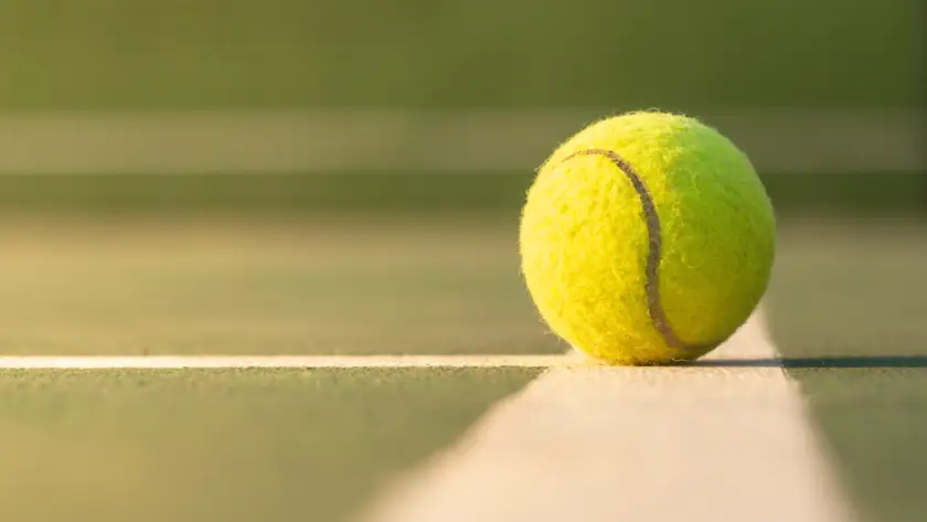 A close-up of a tennis ball on the baseline of a court, illustrating the rich history and evolution of tennis equipment.