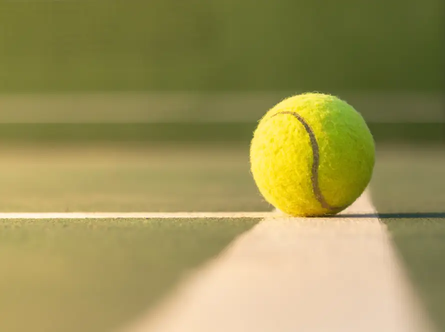 A close-up of a tennis ball on the baseline of a court, illustrating the rich history and evolution of tennis equipment.